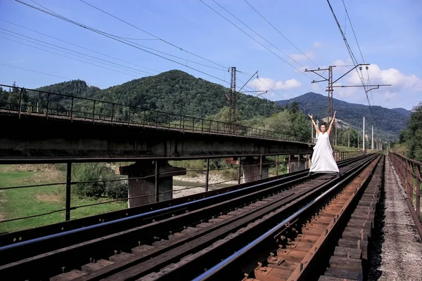 長く美しい白いドレスのブルネット ジョージア州の山岳鉄道 ジョージア州の性質 鉄のレールと Sleepers Way 家に若い女性が立っています — ストック写真