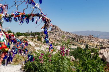 Fotoğrafta, Uchisar adındaki antik bir mağara yerleşiminin arka planına göz şeklinde muskalarla asılı bir ağaç asılıydı..