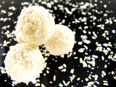 Siyah arka planda Hindistan cevizi taneleri olan lezzetli beyaz çikolata topları.