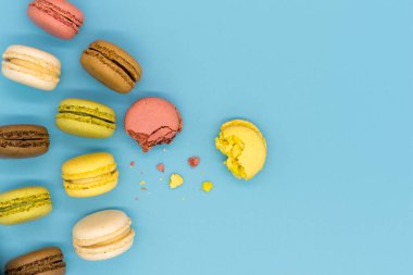 Delicious macarons full and bitten and crumbs arranged on colorful background top view