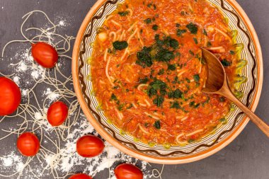 Geleneksel yemekli kil kasesi tahıllı erişteli domateslerden, tahta kaşıktan ve yakınlardaki malzemelerden oluşur.