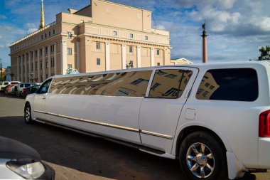 Güneşli bir günde beyaz bir limuzin sokakta duruyor.