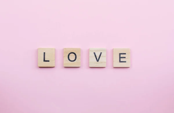 在粉红的背景上拼出爱这个词的文字木块 — 图库照片