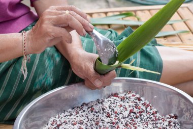 Kadın elleri hindistan cevizi sütü ve muz yaprağında tatlı fasulye ile pirinç katlıyor.