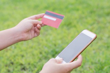 Kadının elinde kredi kartı, cep telefonu ve internet alışverişi için akıllı telefon var. 