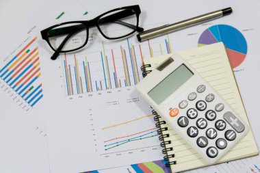 Ofis kavramları: hesap makinesi, gözlük, defter ve kalemle analiz edilen veriler. Sonuçları bulmak için grafikler ve grafikler üzerinde.