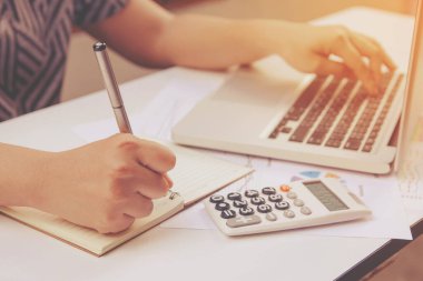 Yazan kadın not alıyor ve ev ofisinde laptop finansmanı kullanıyor..