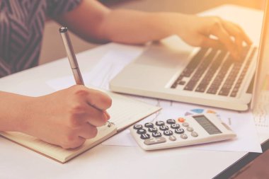 Yazan kadın not alıyor ve ev ofisinde laptop finansmanı kullanıyor..