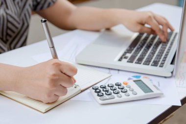 Yazan kadın not alıyor ve ev ofisinde laptop finansmanı kullanıyor..