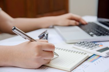 Yazan kadın not alıyor ve ev ofisinde laptop finansmanı kullanıyor..