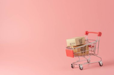 Alışveriş konsepti: pembe arka planda kırmızı alışveriş arabasında karton kutular veya karton kutular. Çevrimiçi alışveriş tüketicileri evden ve teslimat servisinden alışveriş yapabilirler. kopyalama alanı ile
