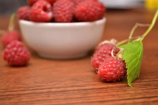 Raspberries in white plate on a wooden table. Raspberry branch. Natural texture. — Stock Photo, Image