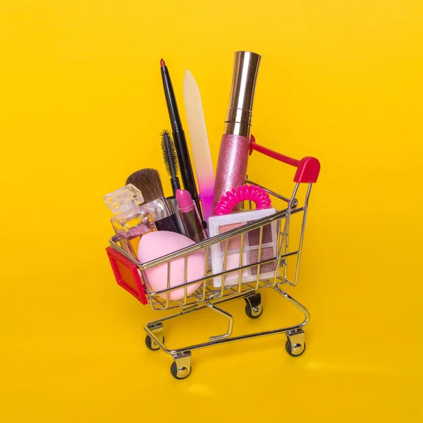 Conceito criativo com carrinho de compras com maquiagem em um fundo amarelo . — Fotografia de Stock