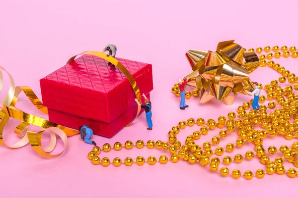 Concepto creativo con personas en miniatura y una caja de regalo sobre un fondo rosa — Foto de Stock