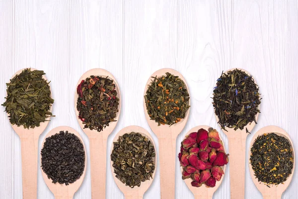 Tahta kaşıklar farklı kuru bitkisel çayların beyaz bir ahşap arka plan ayarla