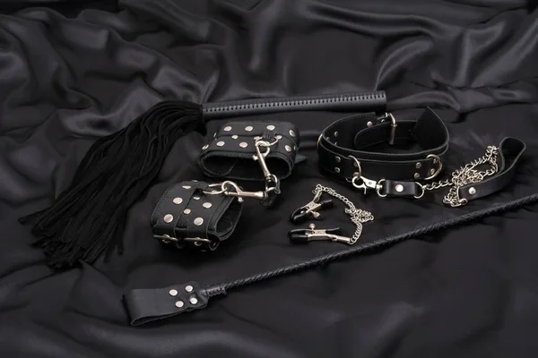 Deri kelepçeler, siyah kırbaç, zincir tasma, meme ucu kıskaçları ve siyah arka plan yığını. Yetişkinler için cinsel oyunlar için aksesuarlar. Bdsm kıyafeti.