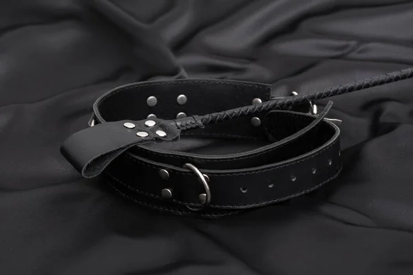 Stack for bdsm games and leather collar on black silk background. Accessories for adult sexual game. Domination concept — Stock Photo, Image