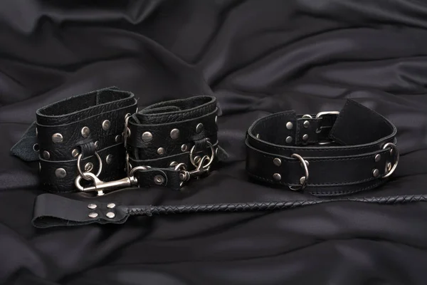 Esposas de cuero, abrazaderas de pezón, collar de cadena y pila sobre fondo de seda negro. Accesorios para el juego sexual para adultos. Equipo BDSM . — Foto de Stock