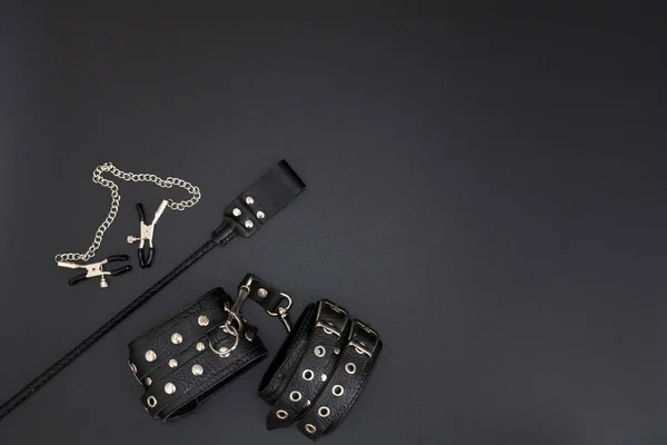 Esposas de cuero, abrazaderas de pezón y pila para juegos BDSM sobre fondo negro. Accesorios para adulto juego sexual —  Fotos de Stock