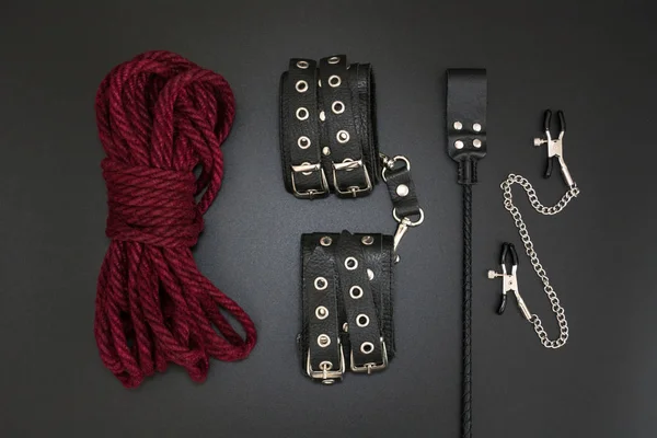 Algemas de couro, corda shibari, grampos de mamilo e pilha para jogos de bdsm no fundo preto. Acessórios para jogo sexual adulto — Fotografia de Stock