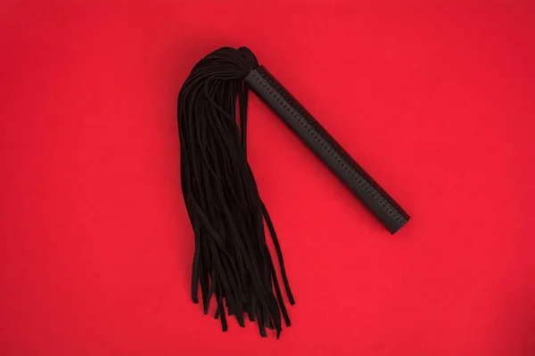 Látigo negro sobre fondo de seda roja. Accesorios para juegos sexuales para adultos. Juguetes para BDSM — Foto de Stock