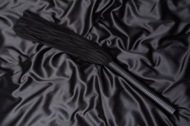 Siyah ipekli arka planda siyah kırbaç. Yetişkinlerin cinsel oyunları için aksesuarlar. Bdsm için Oyuncaklar