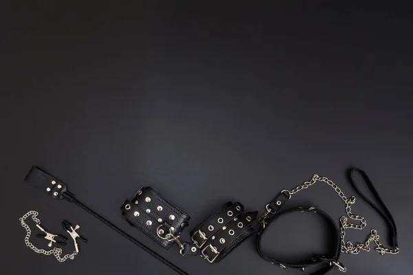 Кожаные наручники, кнут, зажимы для сосков и стопка на черном фоне — стоковое фото