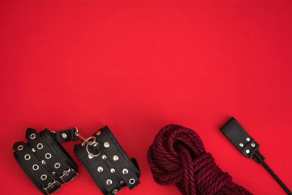 Deri kelepçe, Shibari için ip ve kırmızı arka planda bdsm oyunları için istif. Yetişkinlerin cinsel oyunları için aksesuarlar