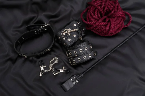 Algemas de couro, corda shibari, grampos de mamilo, colar de corrente e pilha em fundo preto. Acessórios para jogo sexual adulto. Roupa BDSM . — Fotografia de Stock