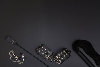 Leather handcuffs, whip, nipple clamps and stack on black background clipart