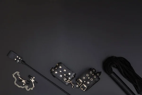 Кожаные наручники, кнут, зажимы для сосков и стопка на черном фоне — стоковое фото