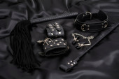 Lederhandschellen, schwarze Peitsche, Kettenkragen, Brustwarzenklammern und Stapel auf schwarzem Hintergrund. BDSM Outfit.