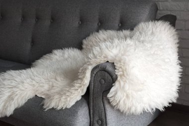 Gri bir kanepede beyaz koyun postu. Evde dinlenmek için rahat bir yer. Modern İskandinav tarzı iç mimari