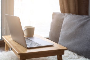 Evden çalışıyorum. Uzaktan kumandalı iş ve iş için pencerenin yanında rahat bir iş yeri. Laptoplu kahve masası. Karantina, koronavirüs konsepti.