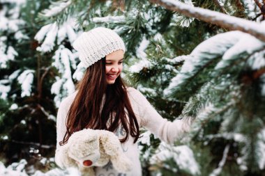 Küçük kız karlı bir kış ormanında yürüyor ve eğleniyor.