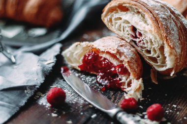 Karanlık bir masada ahududu reçeli ile doldurulmuş kruvasan.