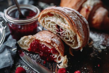 Karanlık bir masada ahududu reçeli ile doldurulmuş kruvasan.