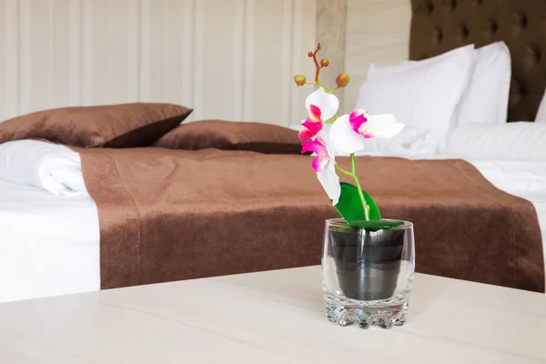 Цветущий искусственный цветок в стекле возле кровати — стоковое фото