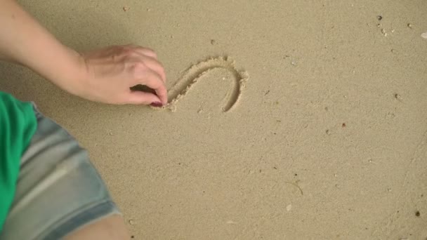 Mujer sentada sola en la playa salvaje y dibujando corazones en la arena — Vídeos de Stock