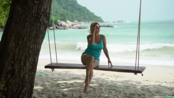 Молодая женщина на качелях на пляже — стоковое видео