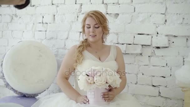Jolie jeune femme blonde en robe de mariée avec bouquet de fleurs posant pour photographe en studio sur fond énorme crème glacée et macaroni En attente dans le terminal de l'aéroport — Video