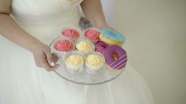 Mujer joven en vestido de novia toma plato con caramelos — Vídeo de stock