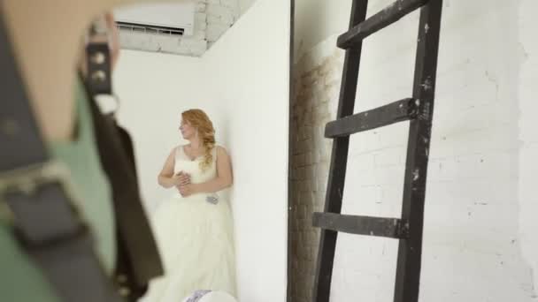 Mignon jeune femme blonde en robe de mariée posant pour photographe en studio steadicam — Video