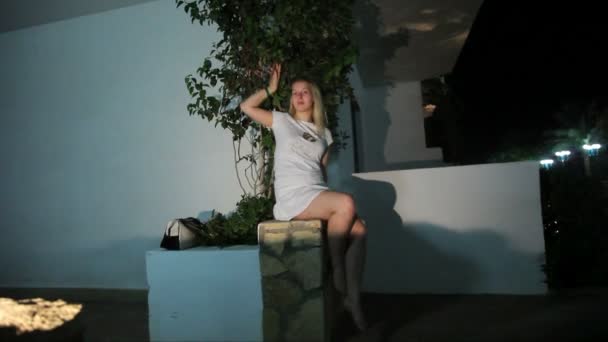 Jonge vrouw zitten buiten in het resort bij nacht — Stockvideo