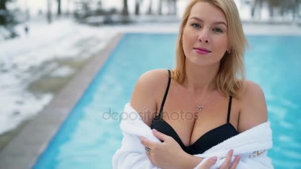 Mujer rubia joven en albornoz cerca de la piscina al aire libre en invierno — Vídeos de Stock