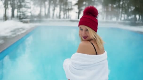 Mladá blond žena v županu a červené boudě u venkovního bazénu v zimě — Stock video