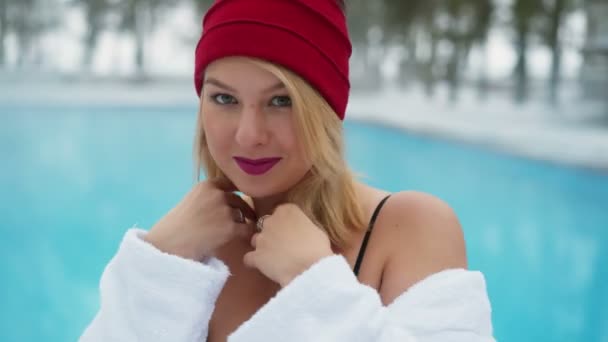 冬の屋外スイミング プールのそばのバスローブと赤の小屋で若いブロンドの女性 — ストック動画
