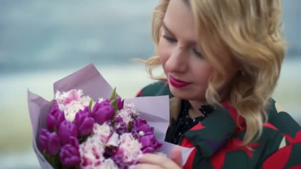 Молодая блондинка с букетиком цветов на городской улице — стоковое видео