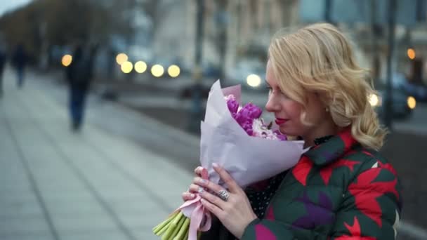 Young blonde woman with flowers bouquet on a city street — Stock Video