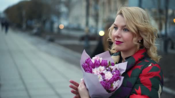 Young blonde woman with flowers bouquet on a city street — Stock Video